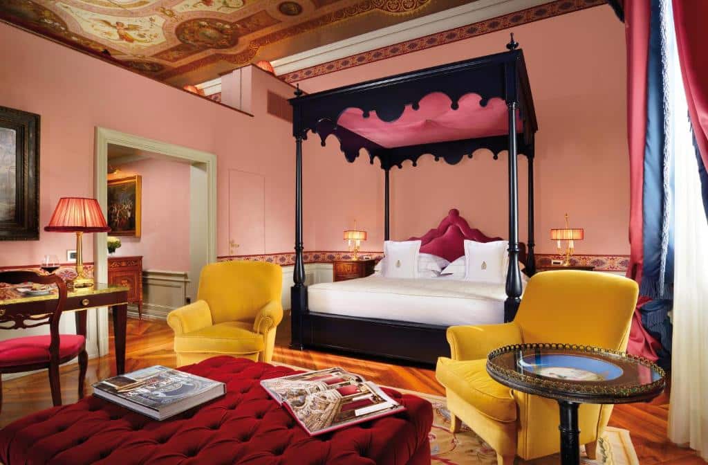 Quarto de decoração clássica do Villa Cora, com 80 m², em tons de vinho, rosa e amarelo, com duas poltronas cor de mostarda, cama de casal grande, mesas de época com candeeiros e uma cadeira estofada
