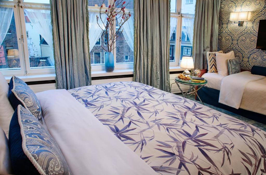 Quarto triplo do Hotel Estheréa, de 22 m², com cama de casal e cama de solteiro, jogo de cama branco e azul, e janelas amplas com vista para um edifício histórico