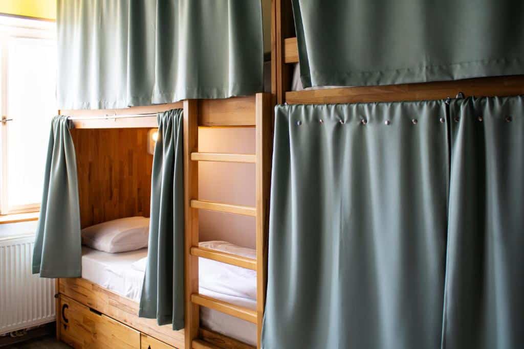 Beliches de madeira com roupa de cama branca e cortinas de privacidade verde-claro fechadas, num quarto bem iluminado do Prague Dream Hostel.