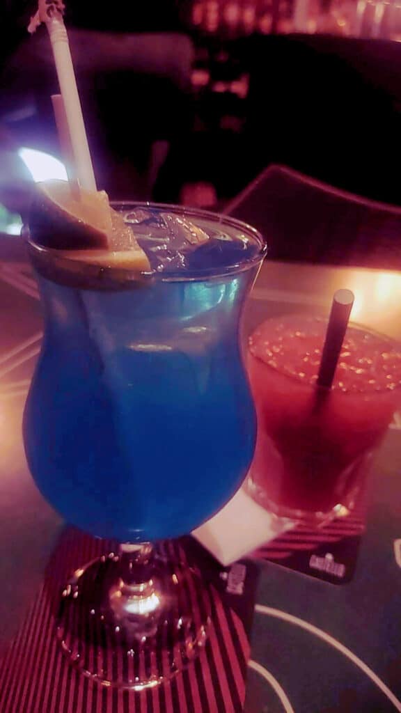 Um cocktail azul com uma rodela de limão e palhinha ao lado de uma bebida vermelha com palhinha, numa mesa no Amuras Bar, em Lagos.