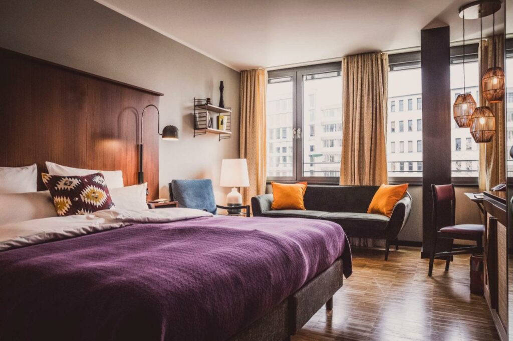 Quarto do Henri Hotel Düsseldorf Downtown com cama de casal, cómoda, poltrona e sofá. Representa hotéis em Dusseldorf.