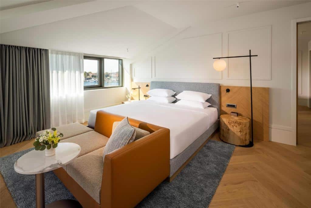 Quarto de hotel moderno com cama de casal, sofá laranja e vista para marina com barcos, no Hyatt Regency Zadar, na Marina