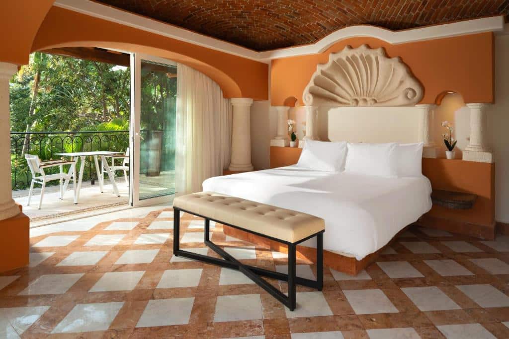 Quarto do Eurostars Hacienda Vista Real com cama de casal ao centro, decoração em tons de laranja e vista para área verde pela varanda.