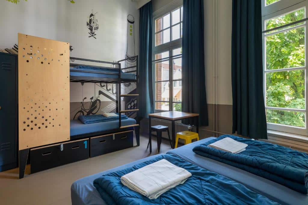 Quarto de albergue do Stayokay Hostel, que ilustra onde ficar em Amesterdão: um beliche, duas camas de solteiro, cacifos, uma secretária, janelas grandes e toalhas dobradas sobre as camas.