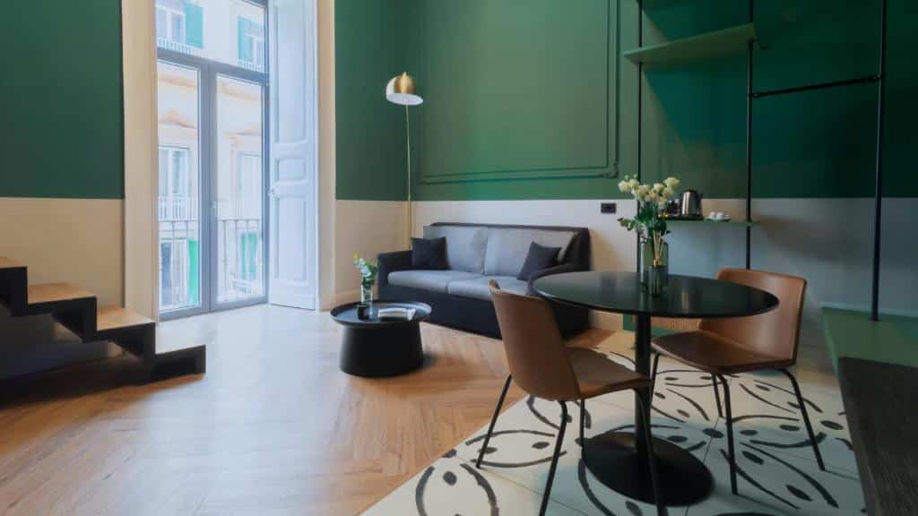 Sofá cinzento numa sala de estar com paredes verdes, mesa de jantar redonda preta e cadeiras de couro castanho, decorada com flores num vaso, no Musto Boutique Apartments.