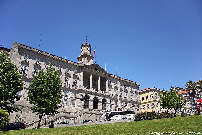 Palácio da Bolsa durante o dia, com um jardim e carros estacionados em frente ao edifício.