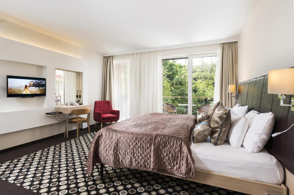 Quarto do Bo33 Hotel Family &amp; Suites com uma cama de casal, TV, secretária, cadeira vermelha, janela grande e alcatifa estampada.