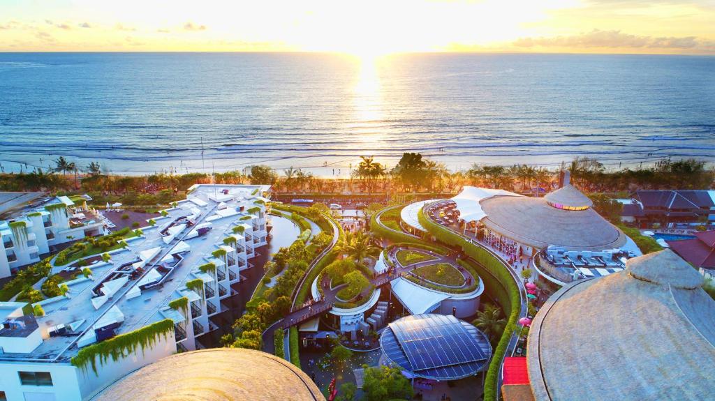 Vista aérea de um hotel moderno perto da praia ao pôr do sol em Kuta, com o oceano ao fundo, em Bali.