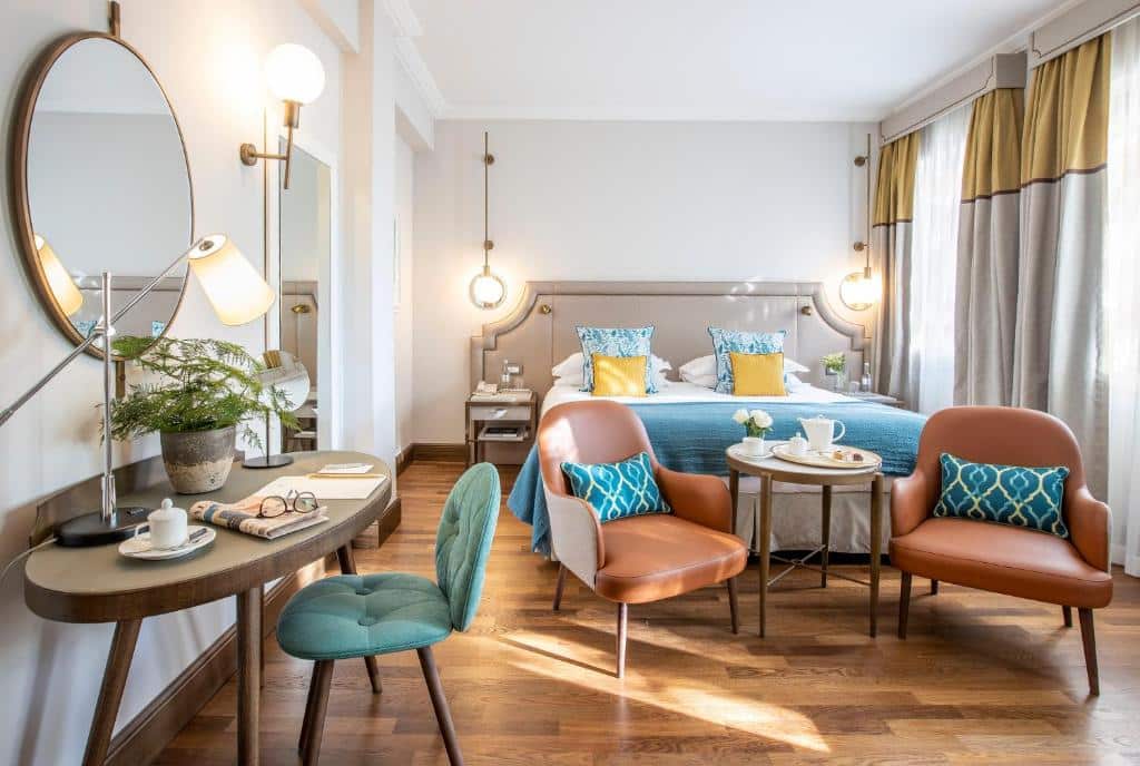 Quarto superior do Terme di Saturnia Natural Spa &amp; Golf Resort, com 18 m², mesa com uma cadeira estofada azul-turquesa, duas poltronas de couro com mesa redonda ao centro, e cama de casal com almofadas e candeeiros ao lado
