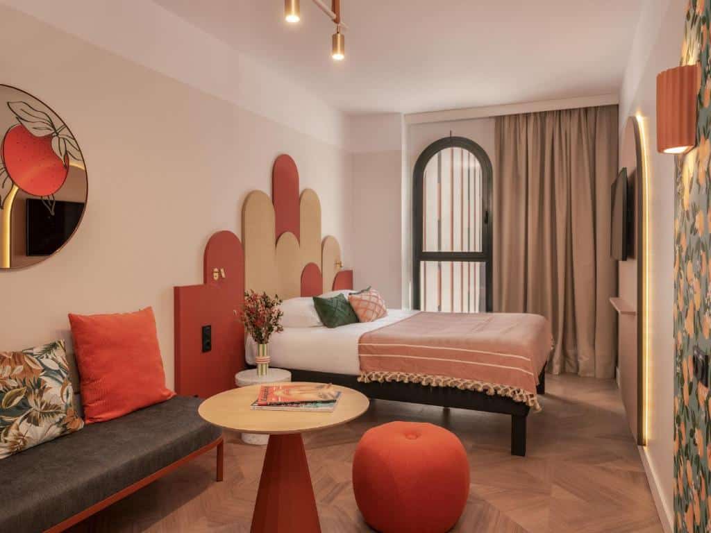 Quarto do Ibis Styles Sevilla City Santa Justa com sofá, cama de casal de cabeceira colorida e televisão.