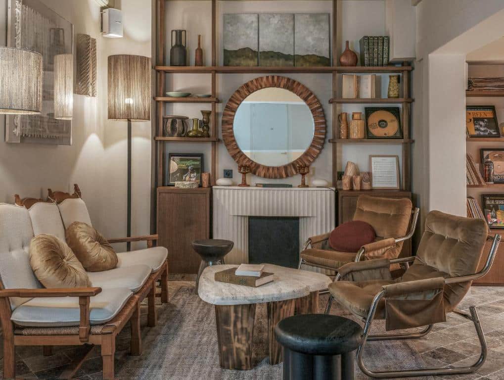 Sala de estar do Hotel Sookie com prateleiras de madeira, espelho redondo sobre a lareira, poltronas e um sofá.