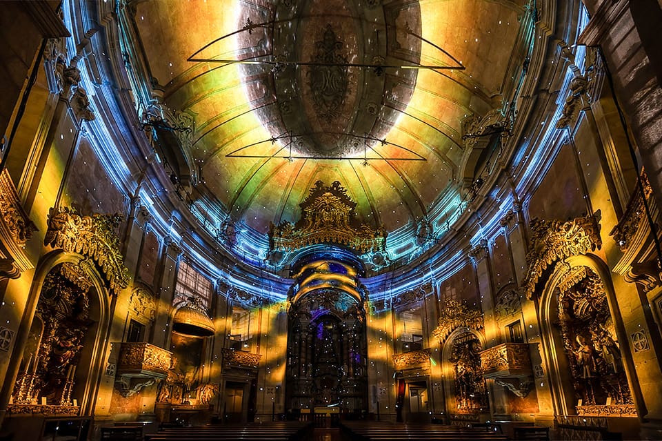 O interior ornamentado da Igreja dos Clérigos, com tetos altos iluminados por luzes coloridas e vibrantes, criando uma atmosfera envolvente.