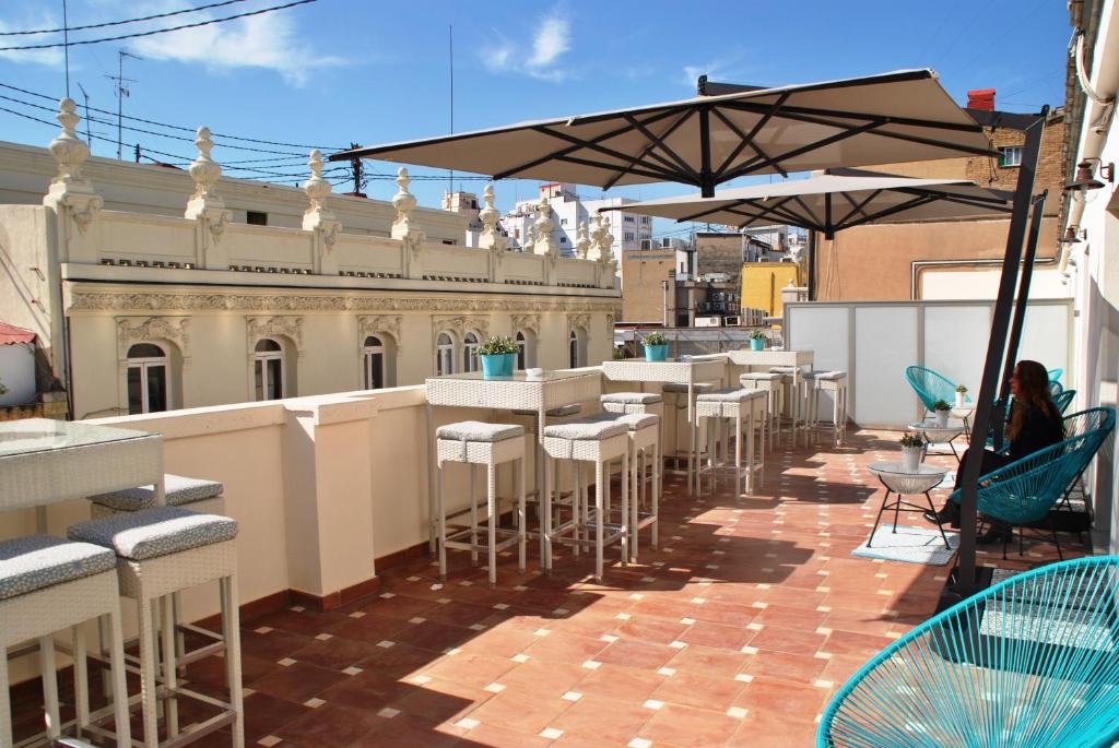 Varanda acolhedora do Vincci Lys, com móveis de vime, mesa alta e cadeiras, guarda-sóis e vista para os edifícios do centro da cidade.