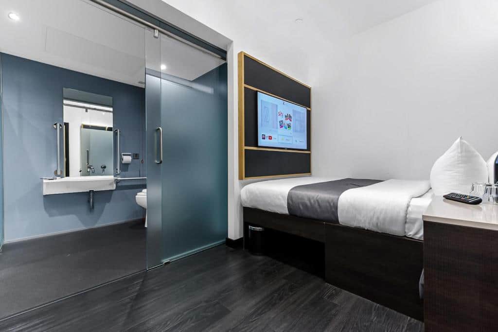 Quarto do The Z Hotel Trafalgar com cama de casal e televisão em frente, mesa de cabeceira e porta de vidro que dá acesso à casa de banho