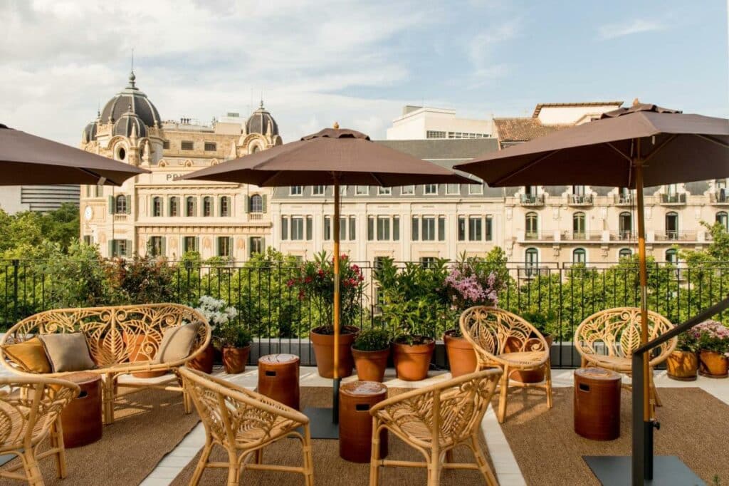 Terraço do Yurbban Ramblas Boutique Hotel, com várias mesas e cadeiras, chapéus de sol castanhos e vasos de flores.