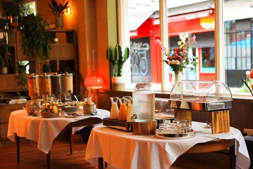 Mesa posta no restaurante do Drury Court Hotel com decoração rústica e plantas verdes, pronta a servir, com sumos, molhos e temperos sobre a toalha cor de laranja.