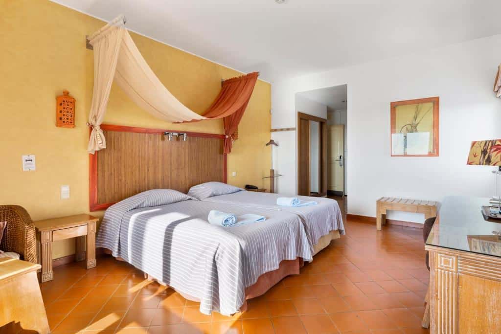 Quarto no Cerro da Marina Hotel em Albufeira, com duas camas de solteiro, roupa de cama às riscas, um dossel e pavimento de azulejo; toalhas colocadas em cada cama.