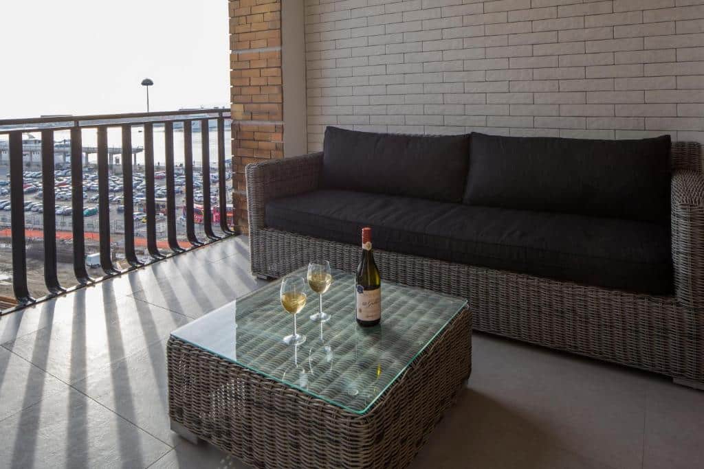Sofá de vime escuro com mesa de centro de vidro numa varanda, com uma garrafa e duas taças de vinho branco na mesa, no Relais Castel Nuovo.