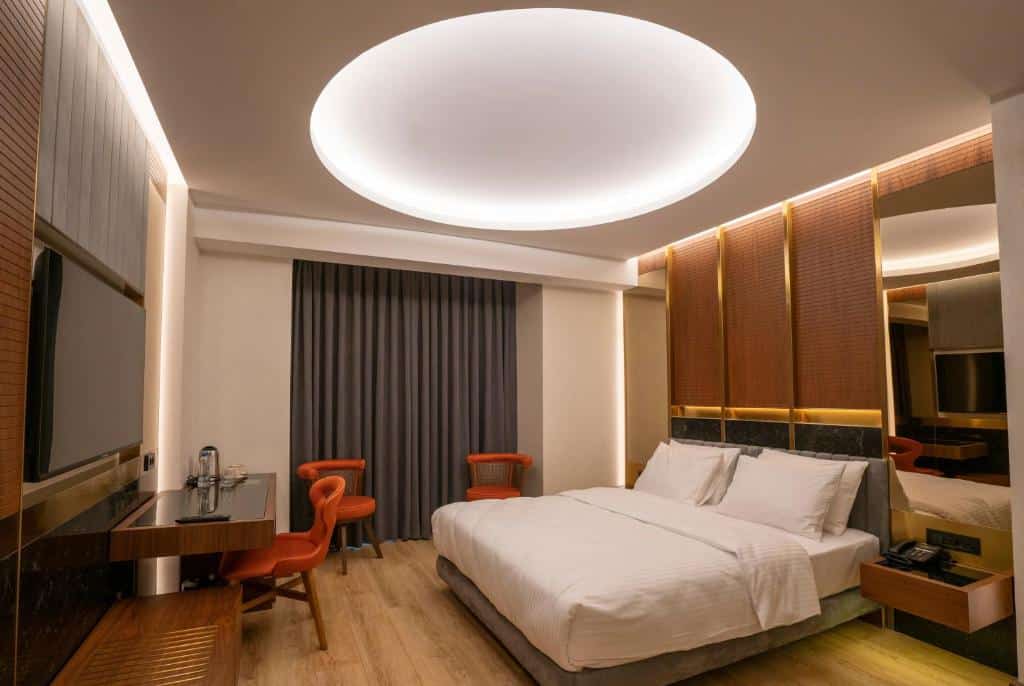 Quarto do Henna Hotel Istanbul com uma cama grande, duas cadeiras vermelhas, uma secretária, uma TV e uma luz de teto circular sobre a cama.