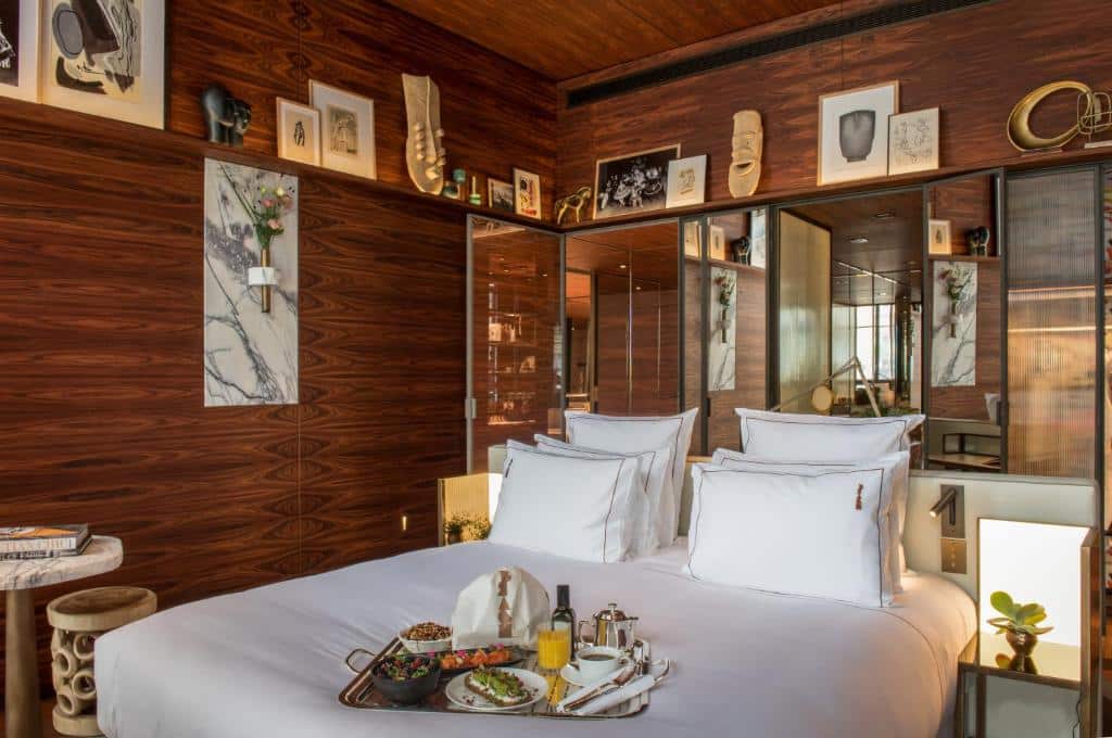 Uma cama bem feita no Brach Paris com lençóis brancos, bandeja de pequeno-almoço e paredes com painéis de madeira decoradas com arte e espelhos.