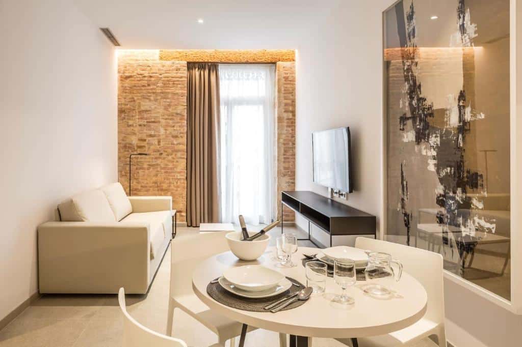 Sala de estar moderna do Mon Suites Benlliure, com parede de tijolo, sofá bege, mesa de jantar redonda com louça, TV na parede e decoração abstrata.