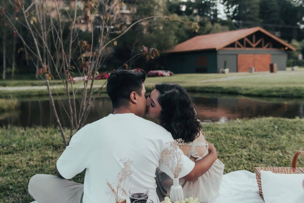 Casal a beijar-se num piquenique romântico ao ar livre com vista para um lago, no parque da Lagoinha em Campos do Jordão