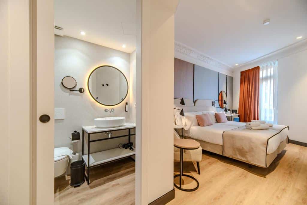 Quarto do Soho Boutique Turia de design minimalista, com cama de casal branca, secretária, espelho circular iluminado e casa de banho adjacente.