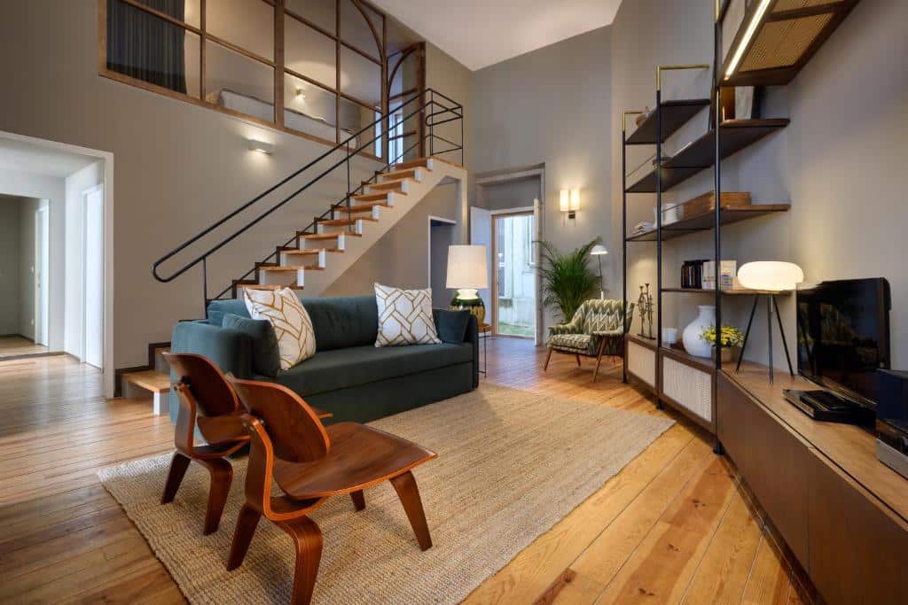 Sala de estar do Condes de Azevedo Palace Apartments, com duas cadeiras de madeira à esquerda, um sofá ao centro e um móvel com TV.