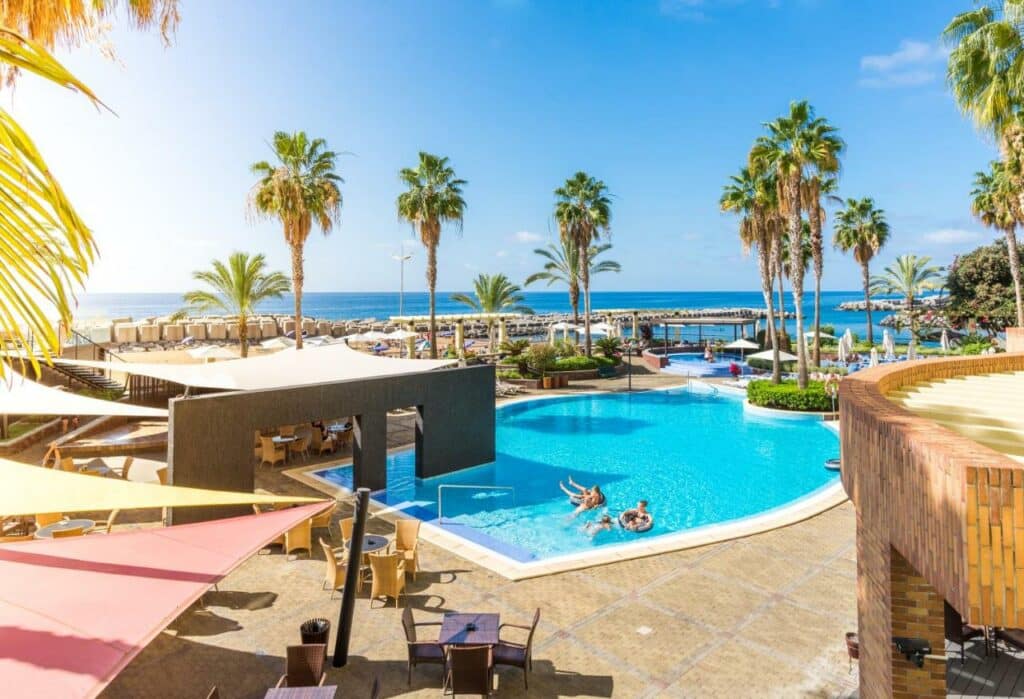 Piscina ao ar livre durante o dia do Calheta Beach - All-inclusive - Savoy Signature com piscina ao centro com três pessoas dentro e ao fundo o mar.