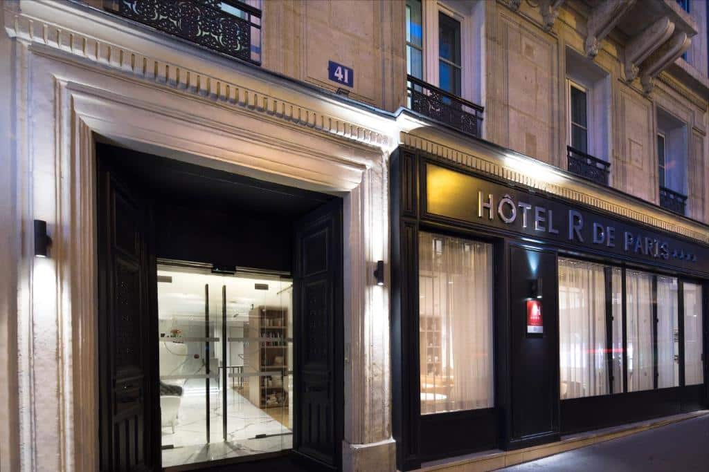 Vista exterior do Hôtel R de Paris à noite, com a entrada iluminada e grandes portas de vidro.