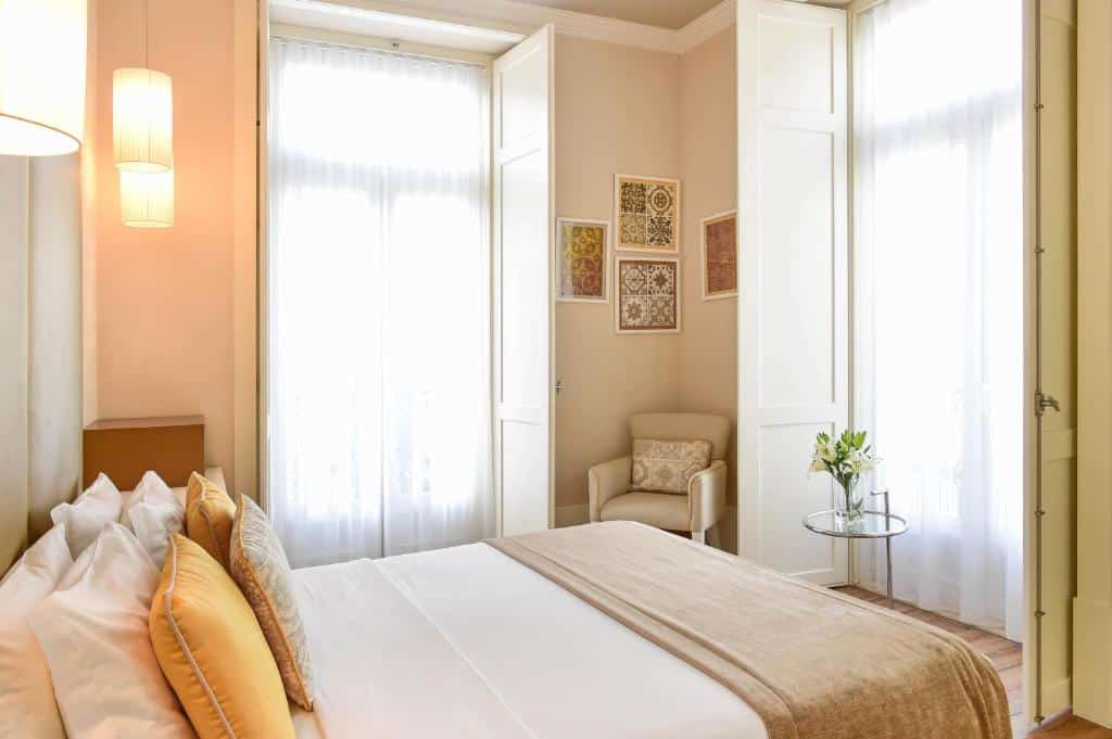 Quarto do My Story Hotel Ouro com duas pequenas varandas com cortinas, uma cama de casal e um cadeirão estofado