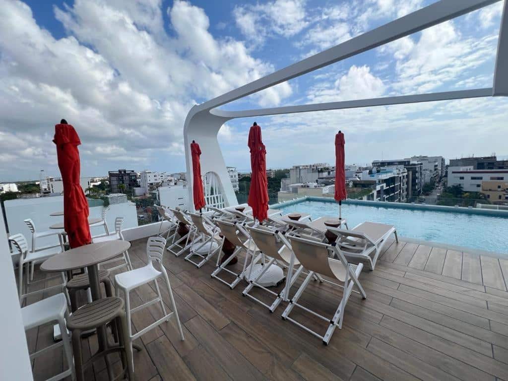 Piscina de bordo infinito com espreguiçadeiras brancas e chapéus de sol vermelhos no terraço de um hotel.