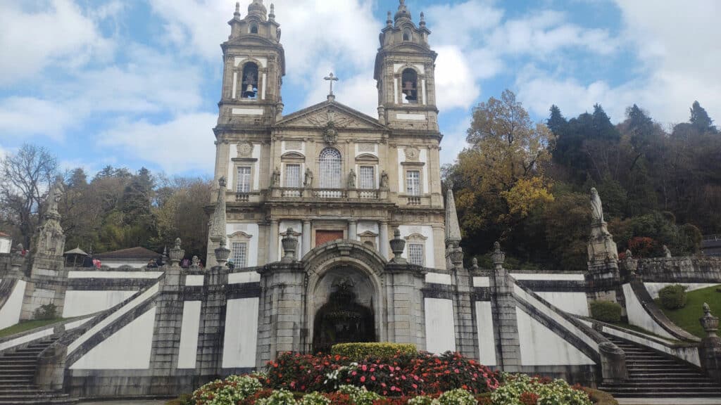 Santuário do Bom Jesus do Monte, em Braga, igreja barroca com torres sineiras gémeas e uma grande escadaria, rodeada de vegetação.