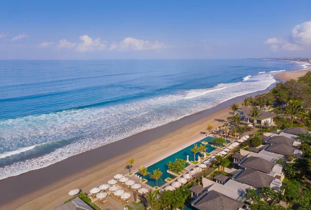 Vista aérea de um resort à beira-mar em Seminyak, com uma piscina comprida, espreguiçadeiras e a praia ao lado, em Bali.