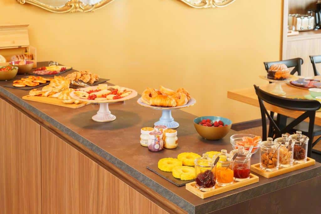 Enorme mesa de pequeno-almoço com uma variedade de guloseimas e pães, incluindo croissants, bolos, fruta e compotas em frascos de vidro, num ambiente acolhedor de paredes amarelas, no Palazzo Pandola.