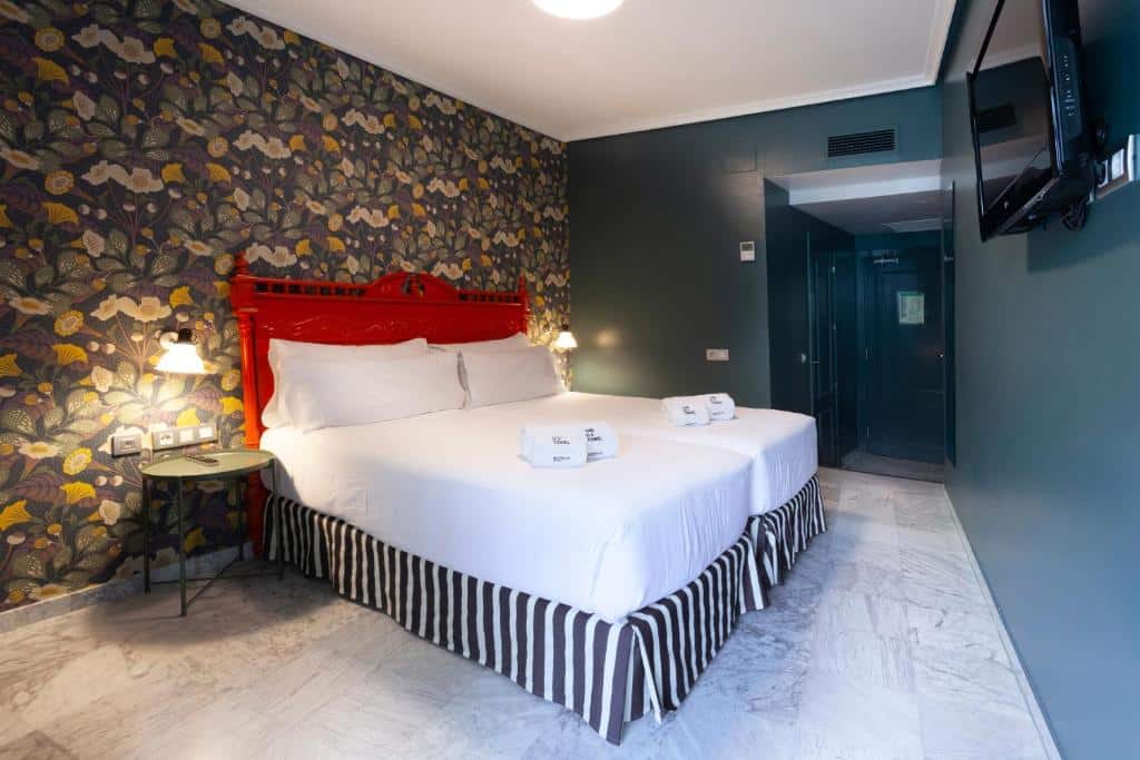 Quarto do Petit Palace Puerta de Triana com cama de casal de cabeceira vermelha e papel de parede florido.
