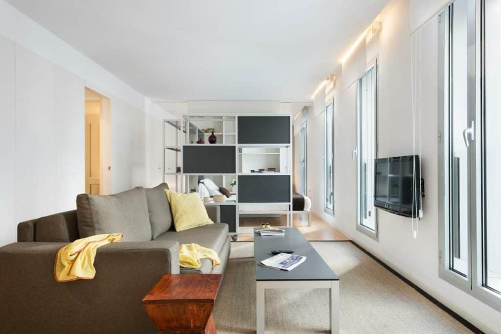 Sala de estar do Lugaris Beach, com sofá castanho, mesa de centro e televisão na parede, num apartamento amplo e luminoso.