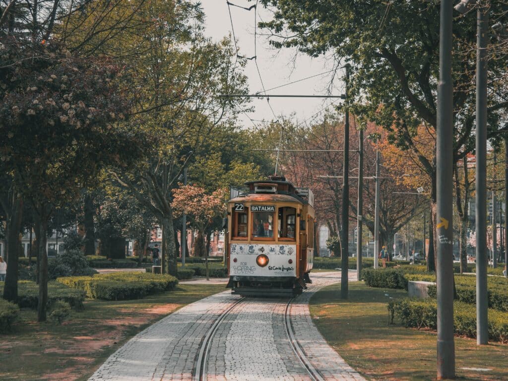 Elétrico a circular no centro da imagem, rodeado por um jardim, no Porto.