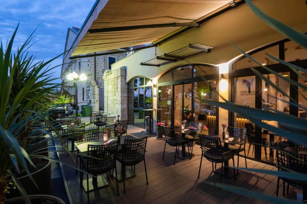Terraço de restaurante com mesas e cadeiras pretas sob toldo retrátil numa noite clara, no Teatro Verdi Boutique Hotel