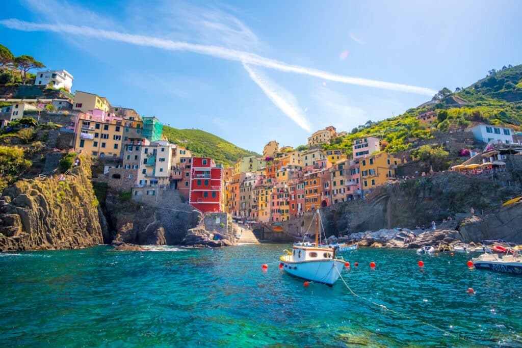 Casas coloridas junto à baía de Riomaggiore, com um barco atracado na água cristalina