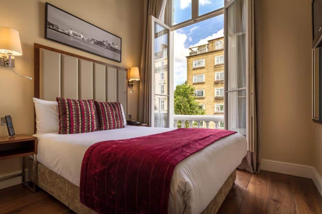 Quarto do The Belgrave Hotel com cama de casal, janela ampla com vista para a cidade, chão em madeira e duas mesas de cabeceira com candeeiros