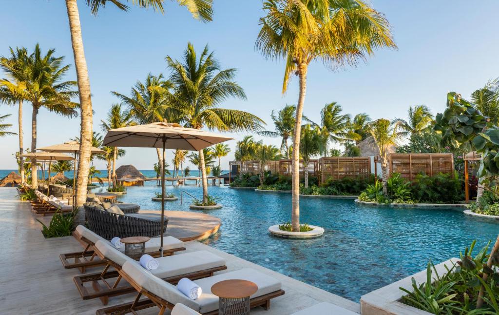 Piscina do Fairmont Mayakoba com espreguiçadeiras, chapéus de sol e palmeiras em dia ensolarado.