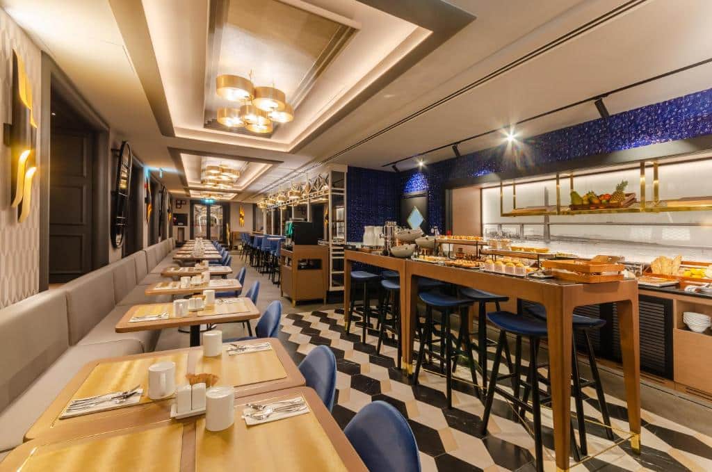Sala de refeições do Eurostars Lisboa Baixa decorada em tons de bege e azul, com bancadas e mesas com itens de pequeno-almoço e pequenos sofás junto de mesas e cadeiras