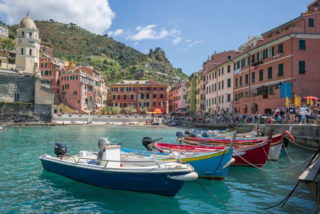 Barcos coloridos no porto de Vernazza, com casas de cores vivas e igreja de cúpula