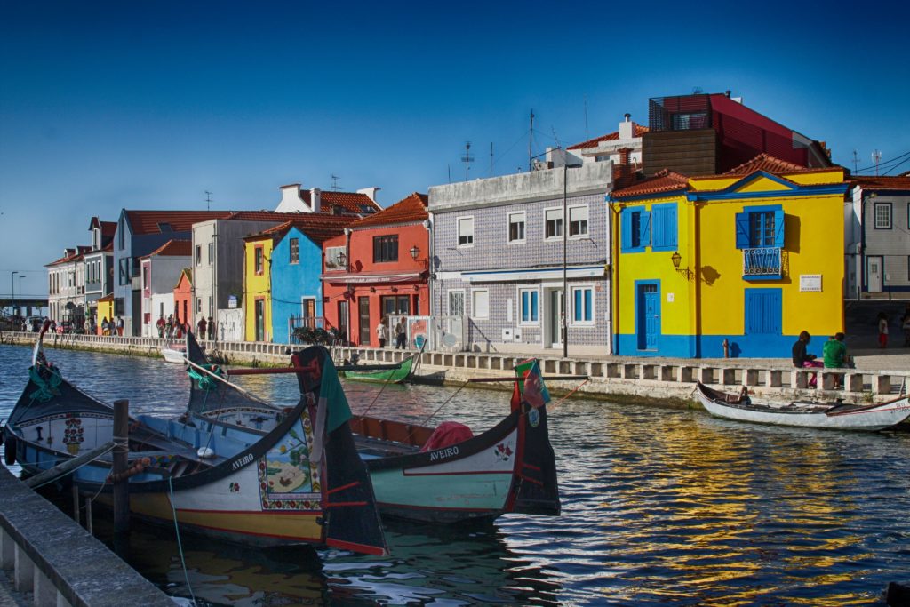 Casinhas coloridas à beira da ria de Aveiro, com barcos moliceiros na água.