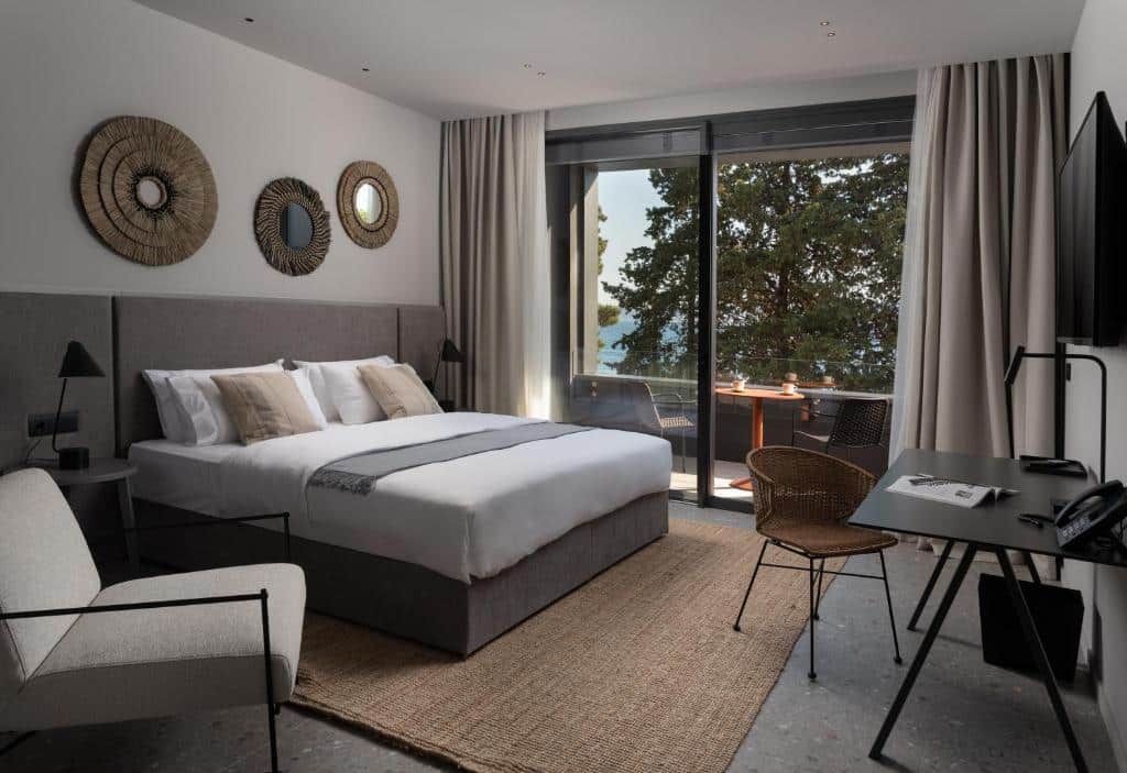 Quarto de hotel moderno com cama de casal, secretária e vista para o mar através de porta de vidro, na La Vista Suites, em Kolovare