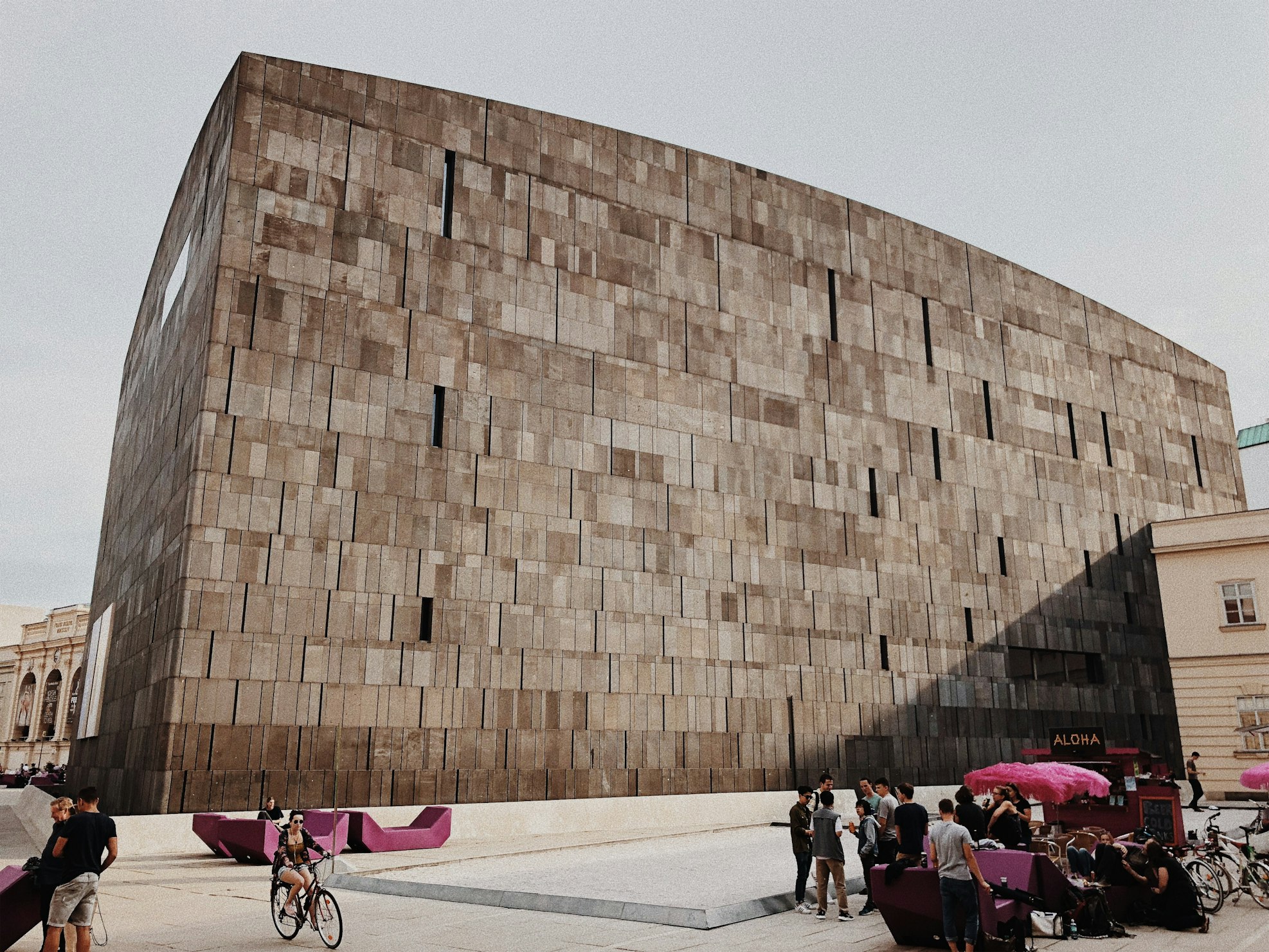 Edifício moderno de betão, em forma cúbica, no Museumsquartier, com pessoas a passear e sentadas em bancos em primeiro plano.