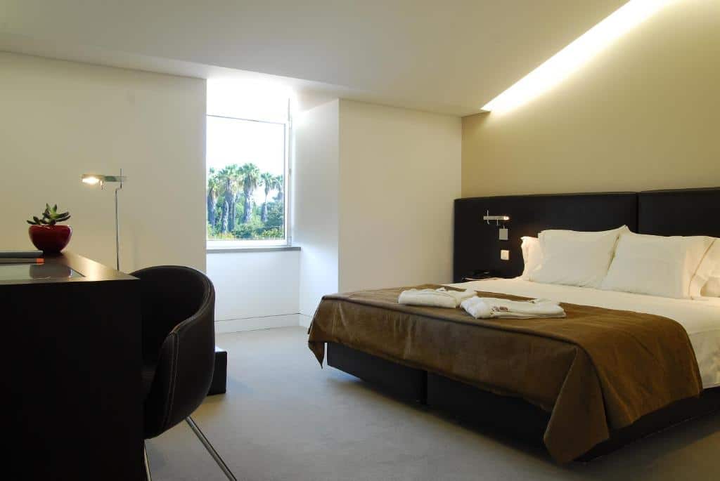 Quarto do Hotel Jeronimos 8 com cama de casal, janela e mesa com poltrona estofada, em Lisboa