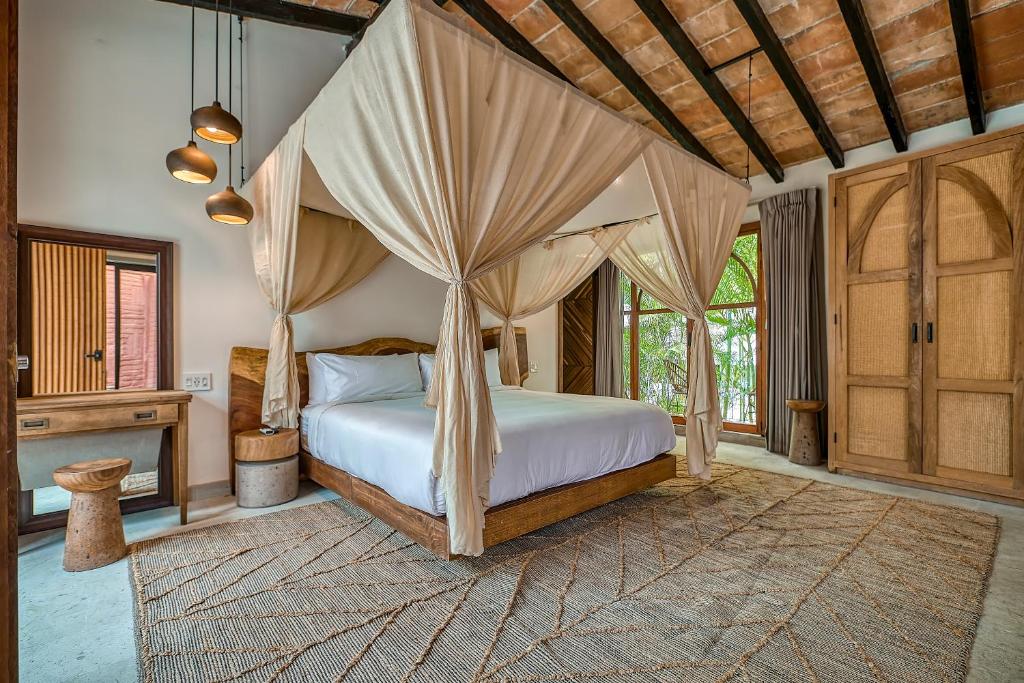 Quarto das Maxwell Residences at Indah com cama de dossel de quatro colunas, móveis de madeira, janelas grandes, candeeiros suspensos e um tapete.