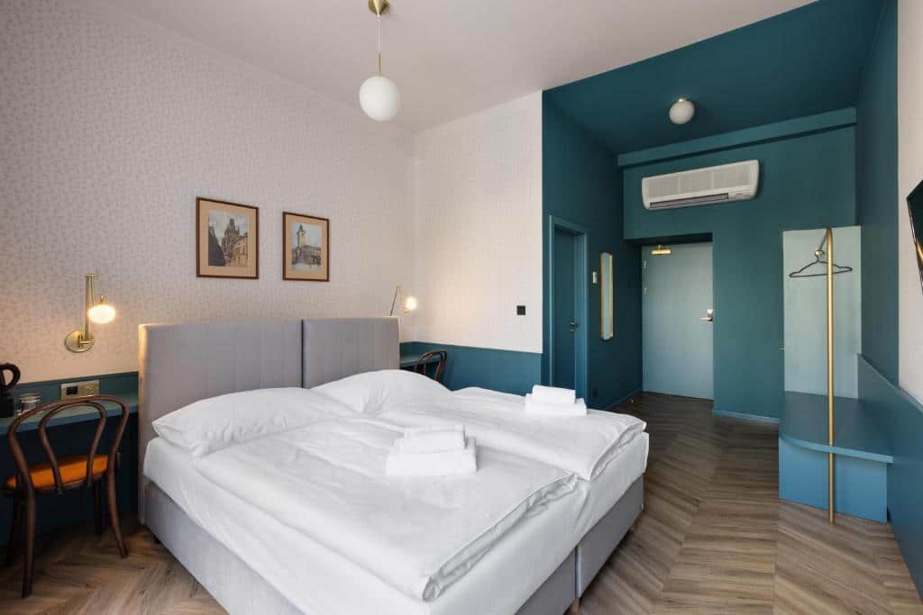 Quarto de hotel moderno do Hotel Beránek, com cama de casal, apontamentos em azul-petróleo, arte na parede, uma secretária e toalhas sobre a cama.